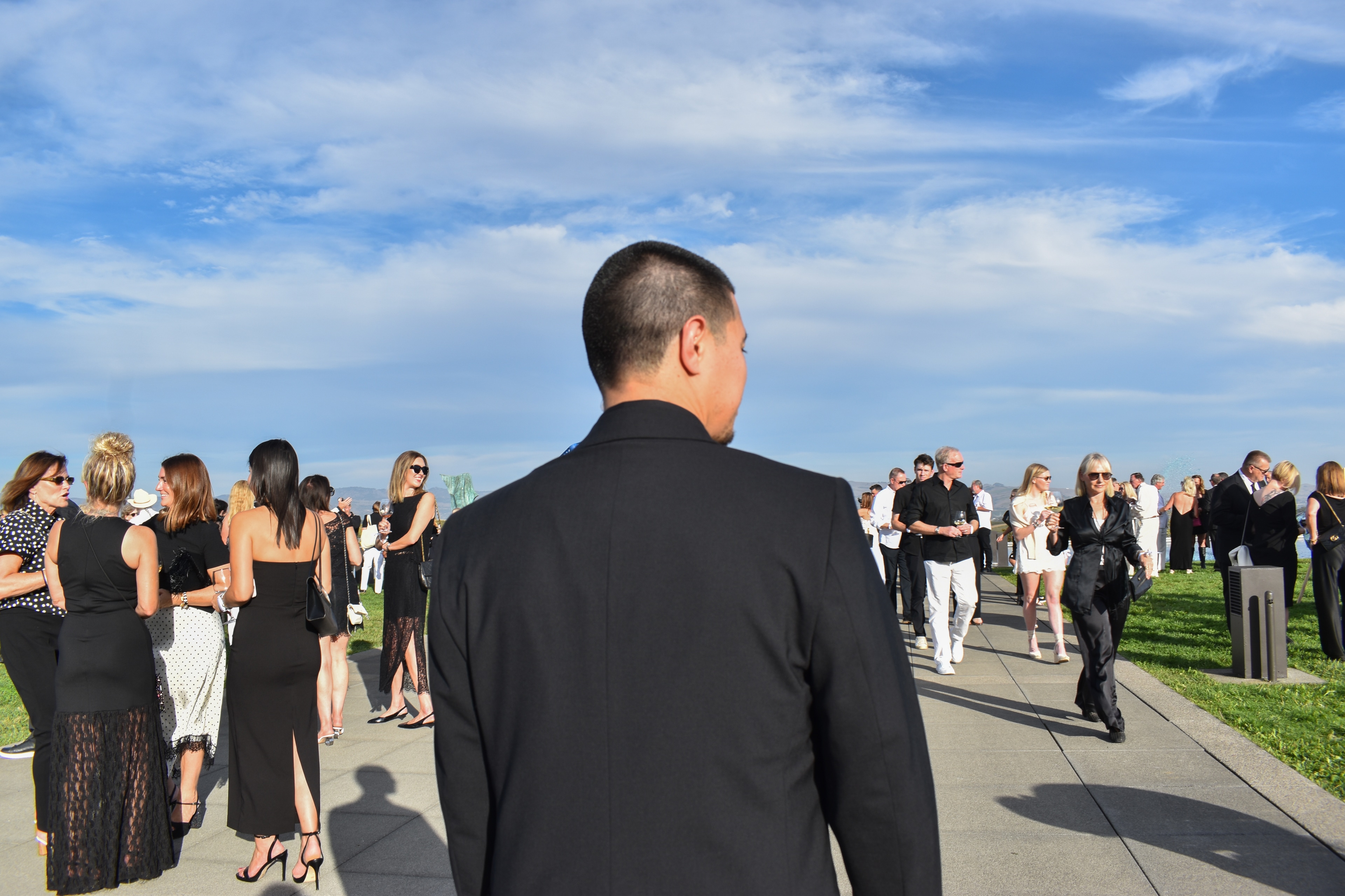 Agent in a dark suit overlooking guests at an outdoor event